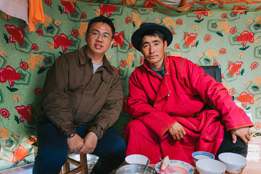 portrait Chinese male tourist and Mongolian man looking at camera smiling sitting inside yurt