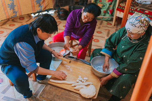 Asian Chinese female tourist learning preparing Mongolian traditional dumpling buuz with local Mongolian women in yurt kneading