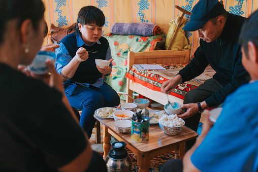 Asian Chinese female tourist enjoying Mongolian traditional meals with local nomad family in yurt
