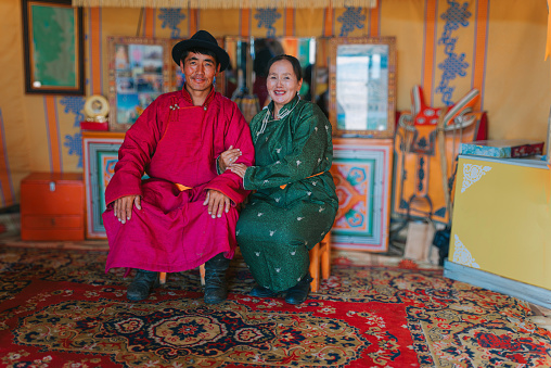 portrait of Mongolian nomad couple with traditional clothing sitting inside Ger, yurt