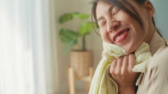 Closeup of beautiful young Asian woman smelling clean clothes and smiling while doing laundry at home. Activity of daily living at house.