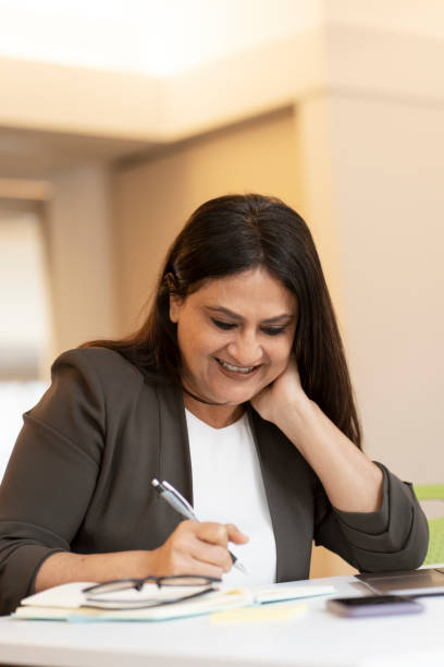 smiling successful mature asian businesswoman, makes notes, works in the office. people and business - multi tasking asian and indian ethnicities asian ethnicity lifestyles imagens e fotografias de stock