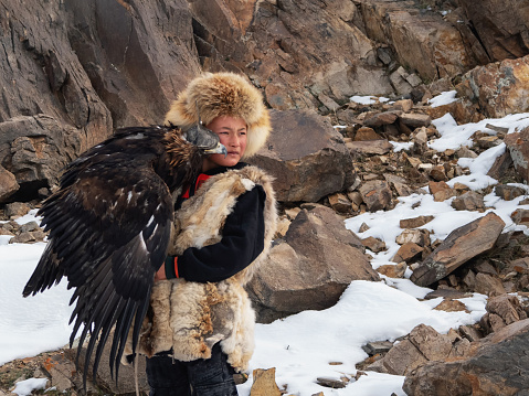Ulgiy, Mongolia - September, 30, 2023: Northern Mongolia. Portrait of a boy with a hunting golden eagle. Eagle hunters are individuals who train and hunt with golden eagles in Mongolia.