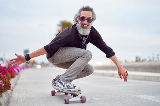 mature man white beard skateboarding on street and having fun