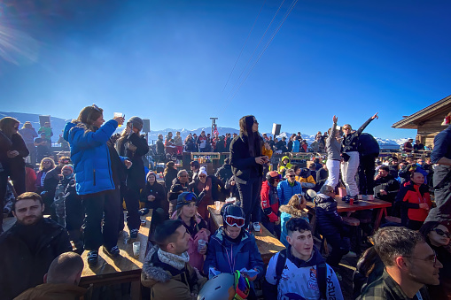 Meribel, France - February 12, 2023: People at apres ski party on the terrace of La Folie Douce, against blue sky