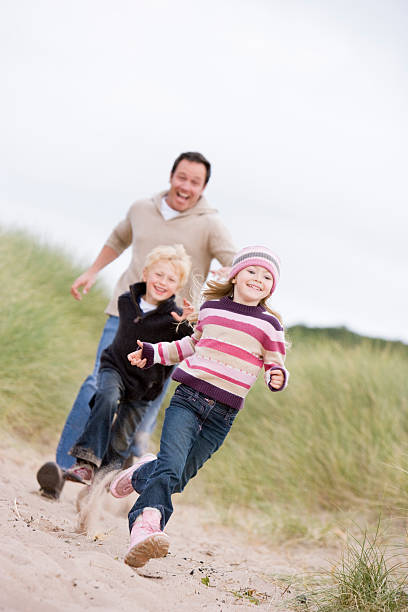 istock Father and two young children running at beach smiling 173726957