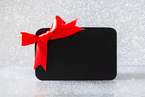 A black gift card with a red bow on a silver glitter background, with copy space.