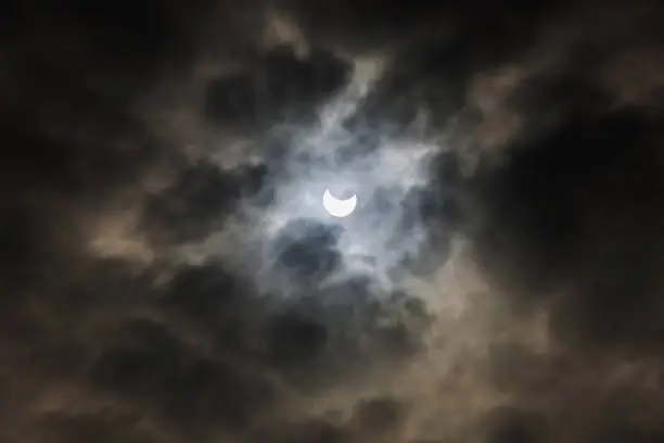 An annular  solar eclipse casts a moody glow through a brooding cloud cover over Corpus Christi, Texas, offering onlookers a dramatic celestial spectacle.