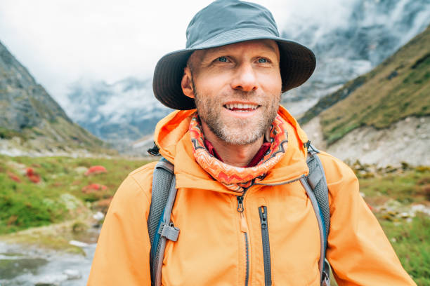 Portrait of smiling Man with backpack dressed orange waterproof jacket and funny hat walking the path during Makalu Barun National Park trek in Nepal. Mountain hiking and active people concept image. retrato de un hombre sonriente con mochila, vestido con una chaqueta impermeable naranja y un sombrero divertido caminando por el camino durante la caminata por el parque nacional makalu barun en nepal. senderismo de montaña e imagen conceptual de persona