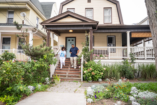 Full length view of casually dressed Black man and woman, smiling as they leave home on summer day in Rockaway Beach, Queens.