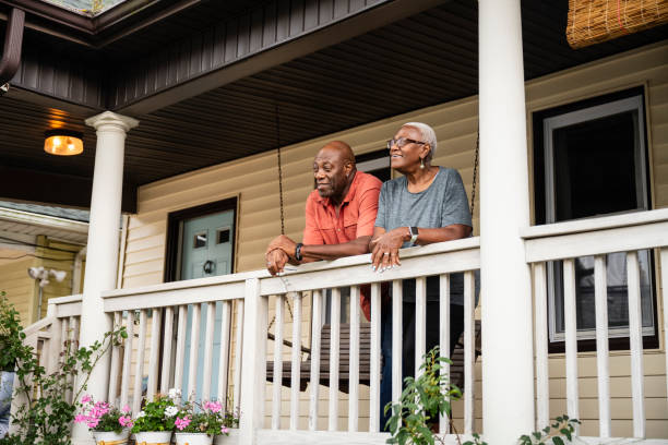 Senior Black couple relaxing on veranda, summer afternoon Three-quarter front view of man and woman in late 60s, casually dressed, leaning on railing, looking away and smiling. house railing stock pictures, royalty-free photos & images