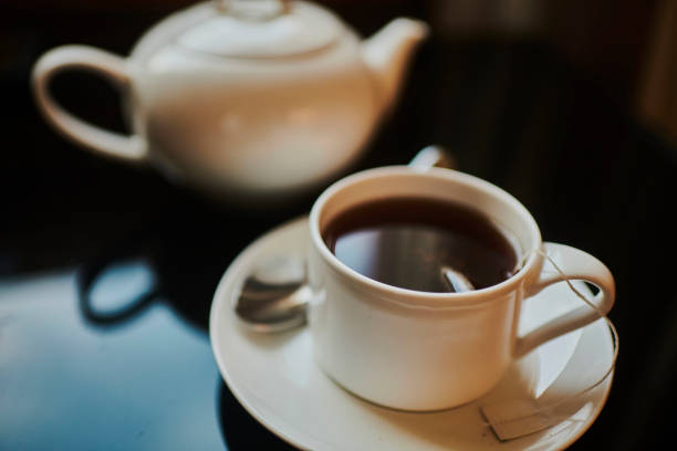 A cup of hot tea served in a white cup and saucer with teapot in the background