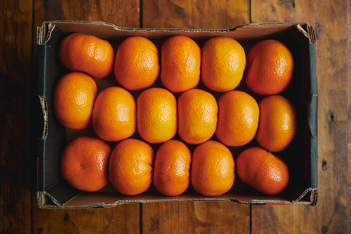 An overhead shot of a box of tangerines on a wooden table - stock photo