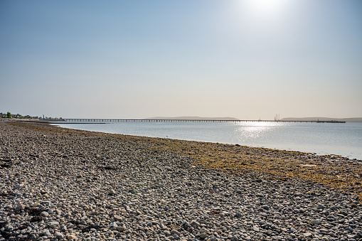Stone beach at Invergordon with long wooden pier at the horizon during sunrise, Scotland