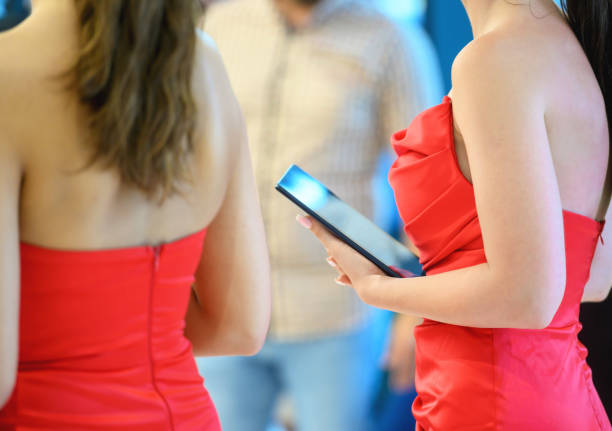 Close-up of unrecognizable young hostesses at a traditional festival. Dressed in formal dresses, they are standing, holding a tablet in their hands.