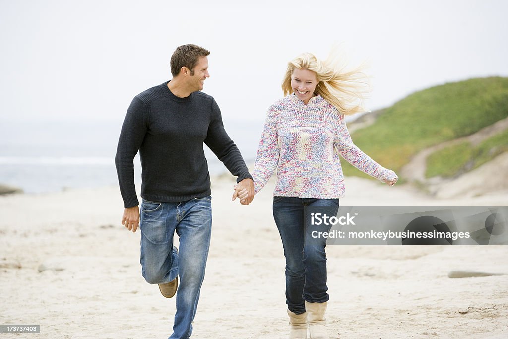 Couple jogging sur la plage tenant les mains souriant - Photo de Activité libre de droits