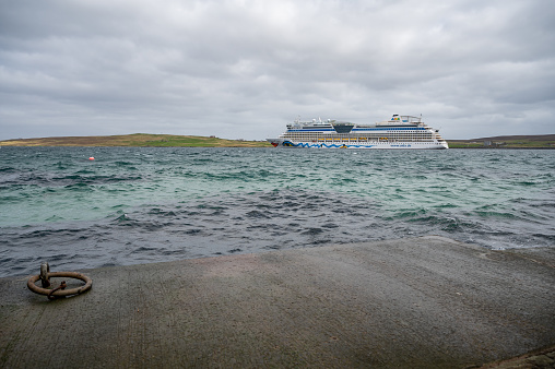 AIDA Bella at Shetland Island with port in front, wide angle shot, side view from the distance during cloudy day