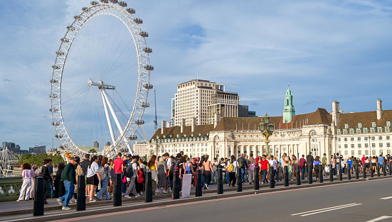 London, United Kingdom - September 12, 2023: View of the London Eye ferris wheel from the Westminster bridge with multiple walking people