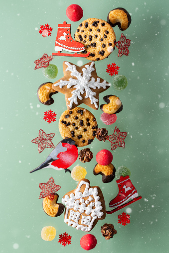 Cookie house and snowflake and marshmallow, decorative skates and bullfinch, stars and marmalade fly among the snow, Christmas levitation, hovering sweets on an olive background