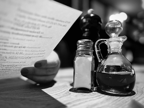 Salt shaker and a glass vinegar bottle next to someone reading a restaurant menu