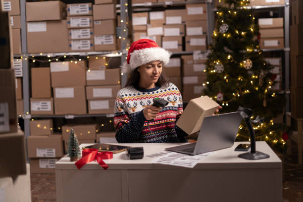 istock Scanning barcode on delivery parcel. Worker scan barcode of cardboard packages on Christmas holiday. Woman in Santa hat working in warehouse scanning labels on the boxes with barcode scanner. 1737468426