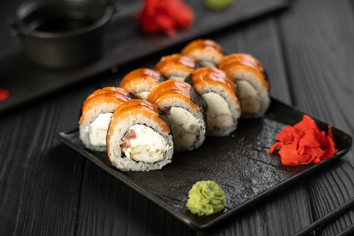 set of sushi and rolls with salmon and tuna, avocado, california, maki, soy sauce, chopsticks close-up on a black stone board on a table. horizontal