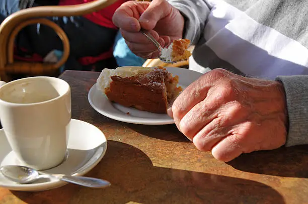 Elderly man (only hands visible) eating a piece of applepie. Coffeecup empty.
