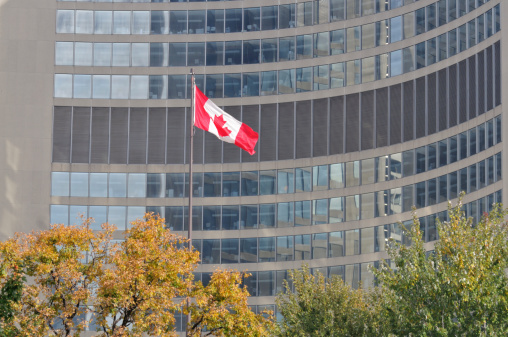 Canadian flag in front of skyscraper, Toronto. Offices can be seen through the glass. Taken in autumn with the trees showing fall colours 
