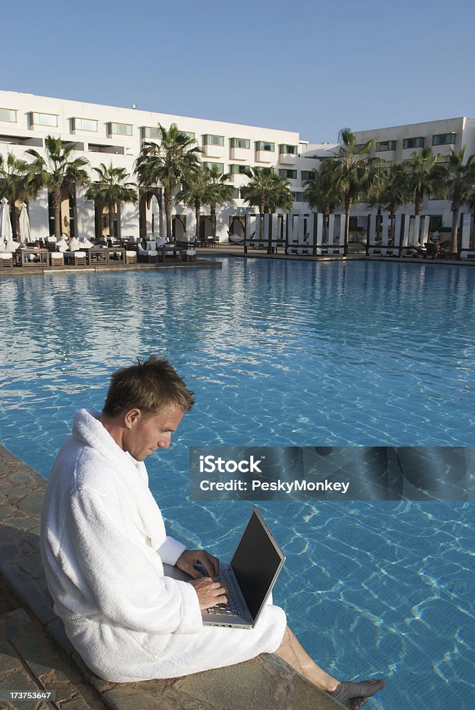 Mann im weißen Bademantel entspannt mit Laptop im Resort Pool - Lizenzfrei Arbeiten Stock-Foto