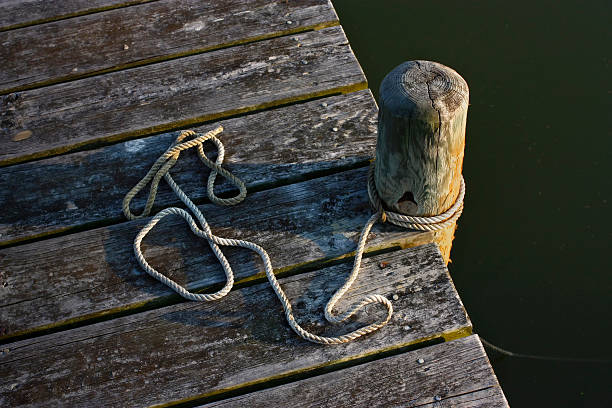 Personal perspective shot of an old weathered boat dock edge overlooking calm dark green marine water of the Chesapeake bay. There is a  white rope attached to the vertical pylon of the pier. The shot is taken at dusk so there is a warm hue and a dramatic shadow and an enhanced texture - A great shot for fresh seafood ingredient Photos or having to do with the fishing industry.