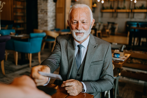 With an air of sophistication, the senior gentleman pays his cafe bill using a credit card, showcasing a seamless and hassle-free approach to modern transactions