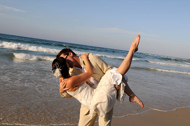 Groom holding his bride on beach