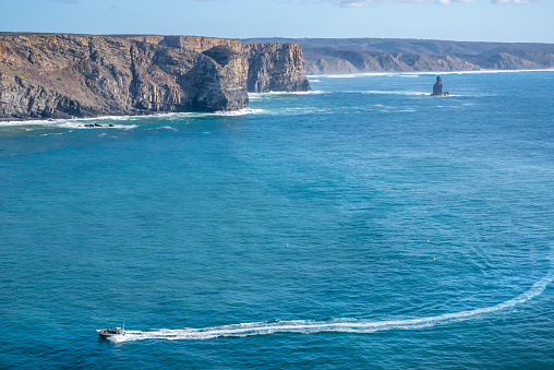 Power Boat sailing in front of the cliffs and rock in the middle of the sea at Arrifana beach, Aljezur, Vicentine Coast, Algarve, Portugal