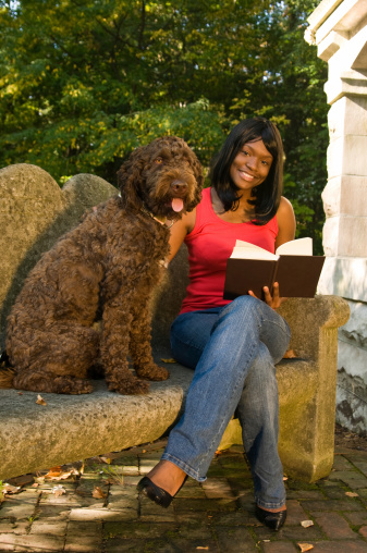 A young woman sitting in the park and reading to her dog (barbet- french water dog)
