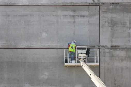 Construction worker in lift truck using tools to work on cured concrete wall of new building.  San Francisco, California, 2009.