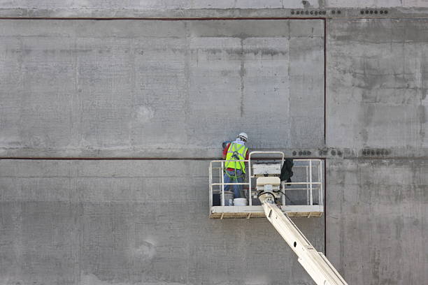 Concrete Worker Construction Equipment Construction worker in lift truck using tools to work on cured concrete wall of new building. San Francisco, California, 2009. concrete work stock pictures, royalty-free photos & images
