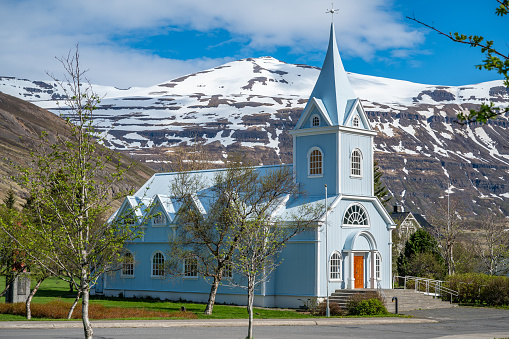 Blue wooden Church at Seydisfjordur, Iceland, view from the side with snow mountains in the background