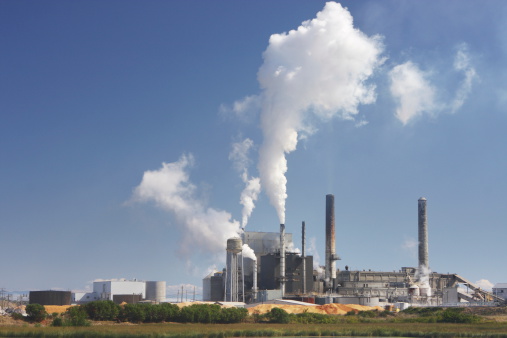 Industrial factory smoke stacks emits polluting smoke into blue sky.