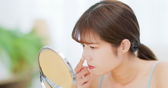 asian upset woman looking her bad unhealthy skin in mirror