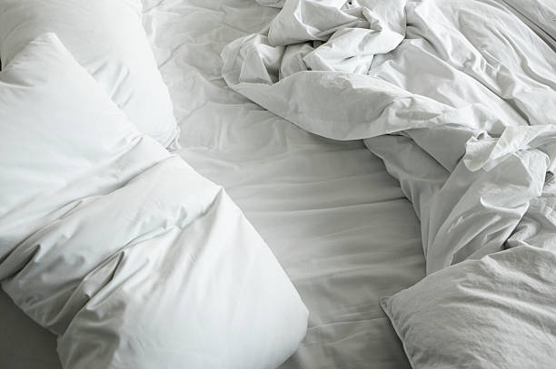disheveled lenzuola e cuscini di un letto sfatte - lenzuolo foto e immagini stock