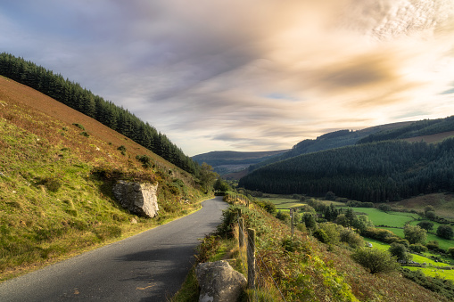 Winding road leading through a mountain valley with forest and farms on the sides in Wicklow Mountains