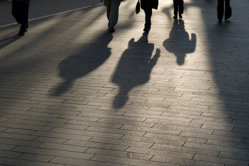 Group of businessmen commuters walks into a sliver of morning light, their shadows preceding them