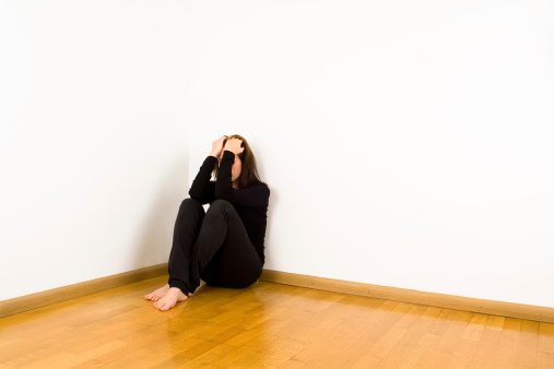 Woman sitting in the corner with the head in her hands