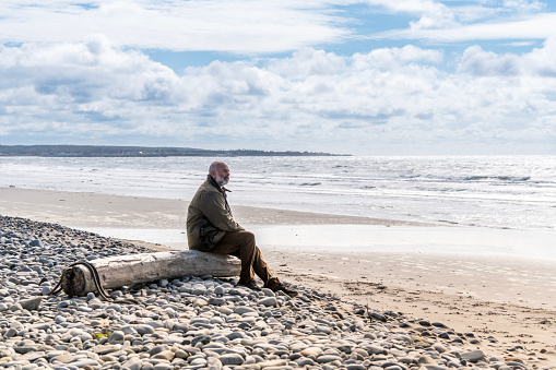 A senior man on a beach in the autumn enjoying the healing power of nature.