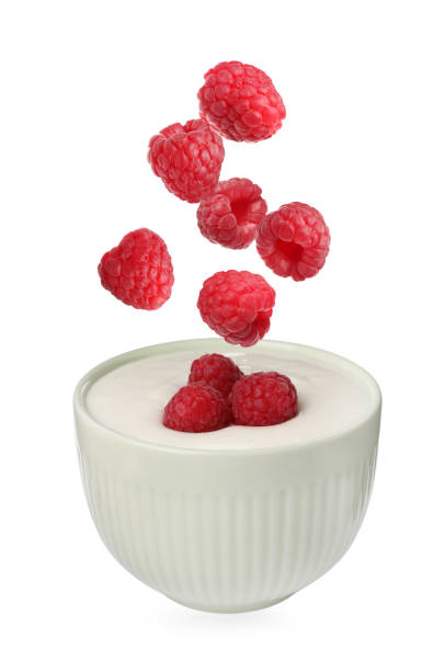 istock Delicious ripe raspberries falling into bowl with yogurt on white background 1737693947