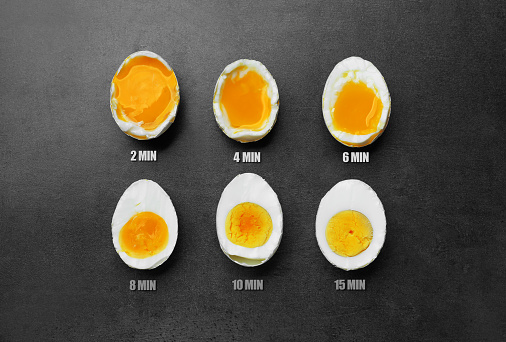 Different readiness stages of boiled chicken eggs on dark grey table, flat lay