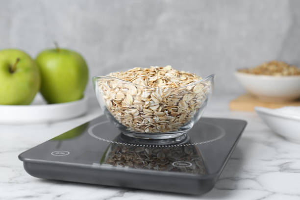 istock Digital kitchen scale with oat flakes on white marble table 1737695684