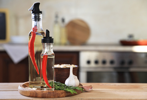 Backlit decorative bottles of herb infused oils and vinegars with the herbs alongside.