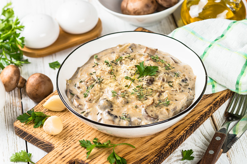 Champignons in cream sauce with herbs and cheese at white table.