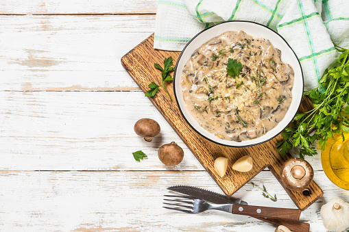 Champignons in cream sauce with herbs and cheese. Top view at white table with ingredients for cooking.
